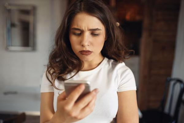serious-attractive-young-woman-holding-smart-phone-frowning-reading-sad-news